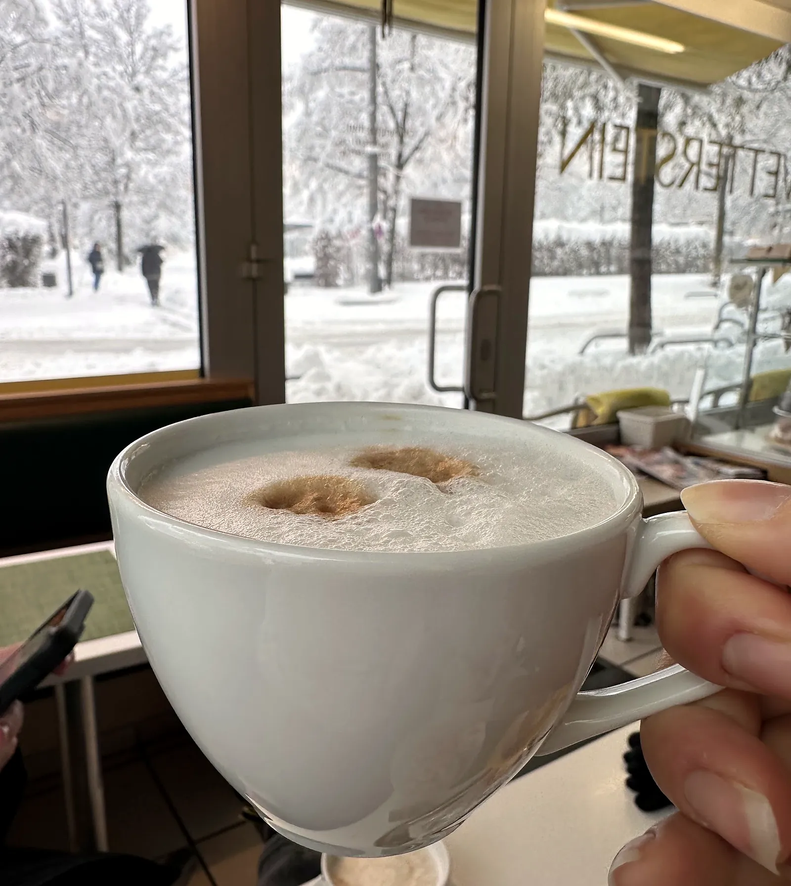 Cappuccino am Fenster mit dem Schriftzug Wetterstein, draußen liegt Schnee