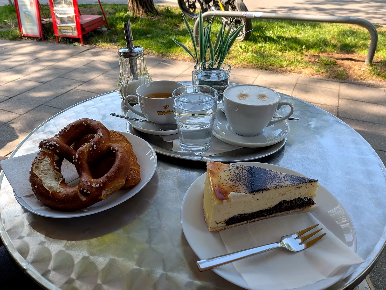 Draußen am runden Tisch: Breze, Käsekuchen, Cappuccino und Espresso