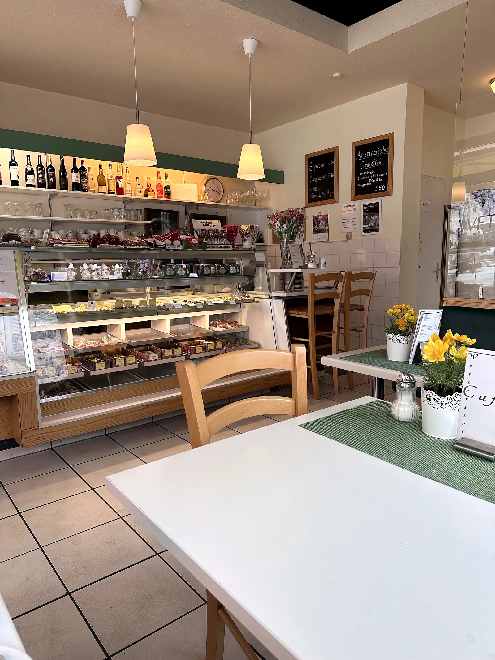 Gastraum mit hellen Tischen, Blumen und der Kuchenvitrine