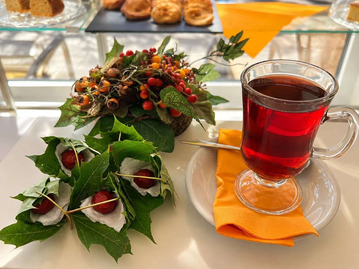 Pralinen, einzeln in grüne Blätter gewickelt, daneben ein Herbstgesteck und ein Glas Glühwein auf Untertasse mit oranger Serviette